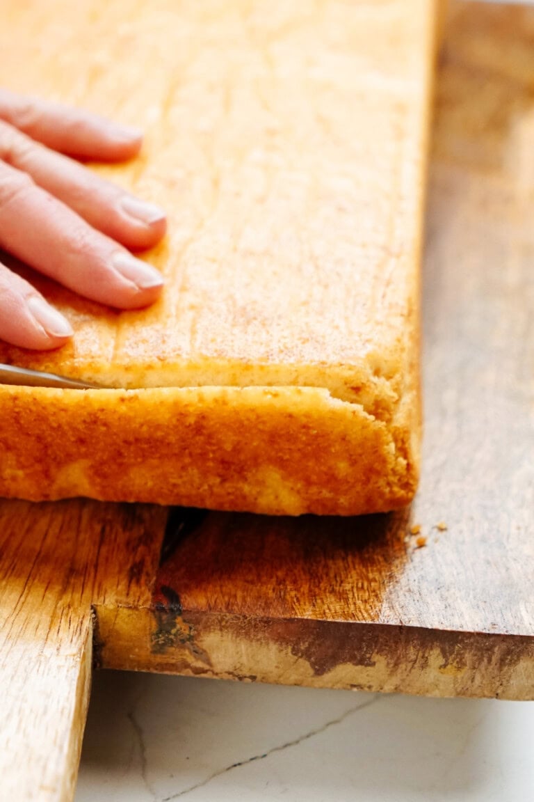 A person's hand is pressing down on a rectangular, golden-brown bread positioned on a cutting board, reminiscent of the treats enjoyed during the festive season like Christmas cake pops.