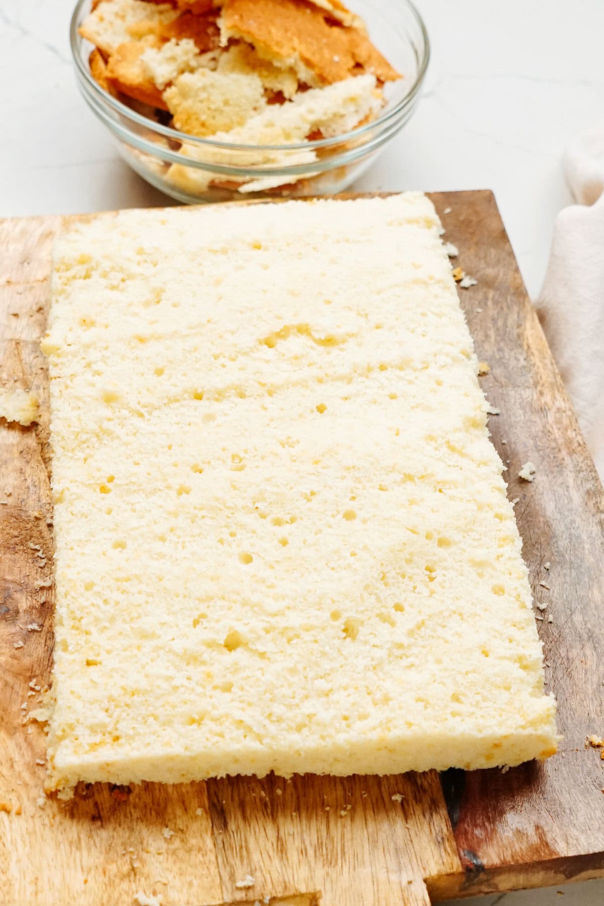 A rectangular piece of sponge cake sits on a wooden cutting board, with a bowl of cake crumbs beside it, ready to be transformed into festive Christmas cake pops.