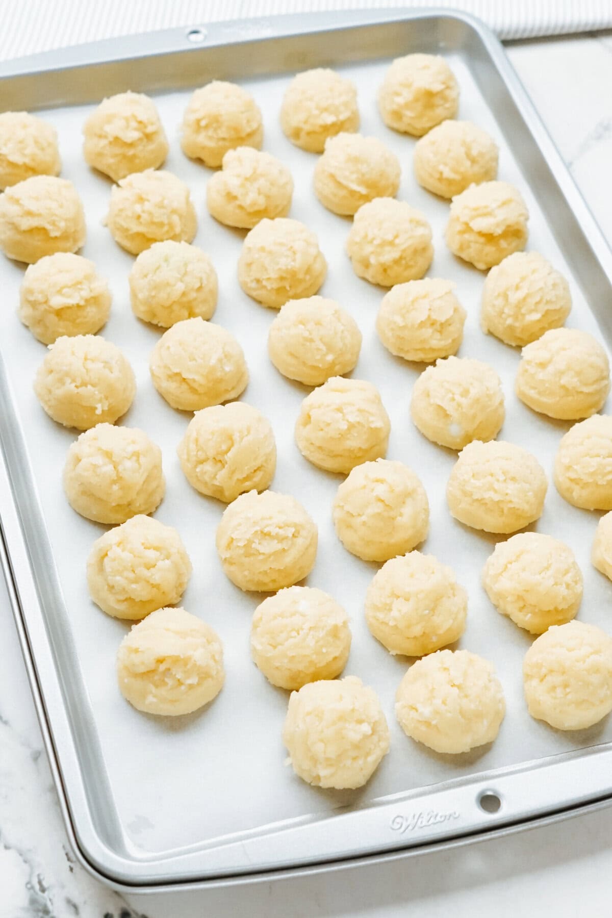 A baking tray with multiple round scoops of cookie dough, perfect for transforming into festive Christmas cake pops, evenly spaced on a sheet of parchment paper.