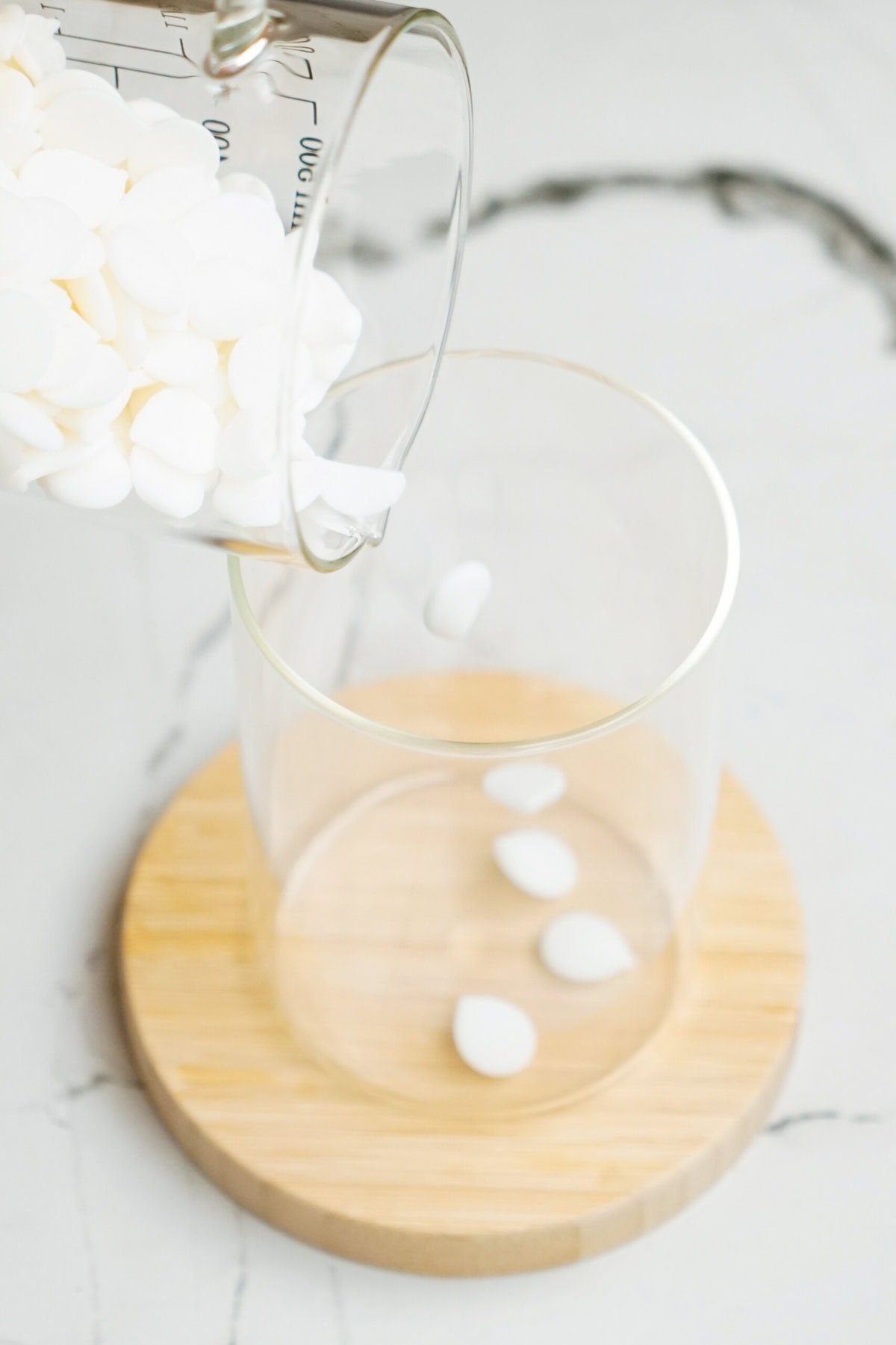 White tablets being poured from a measuring glass into a clear glass container on a wooden coaster evoke the precision of baking Christmas cake pops.