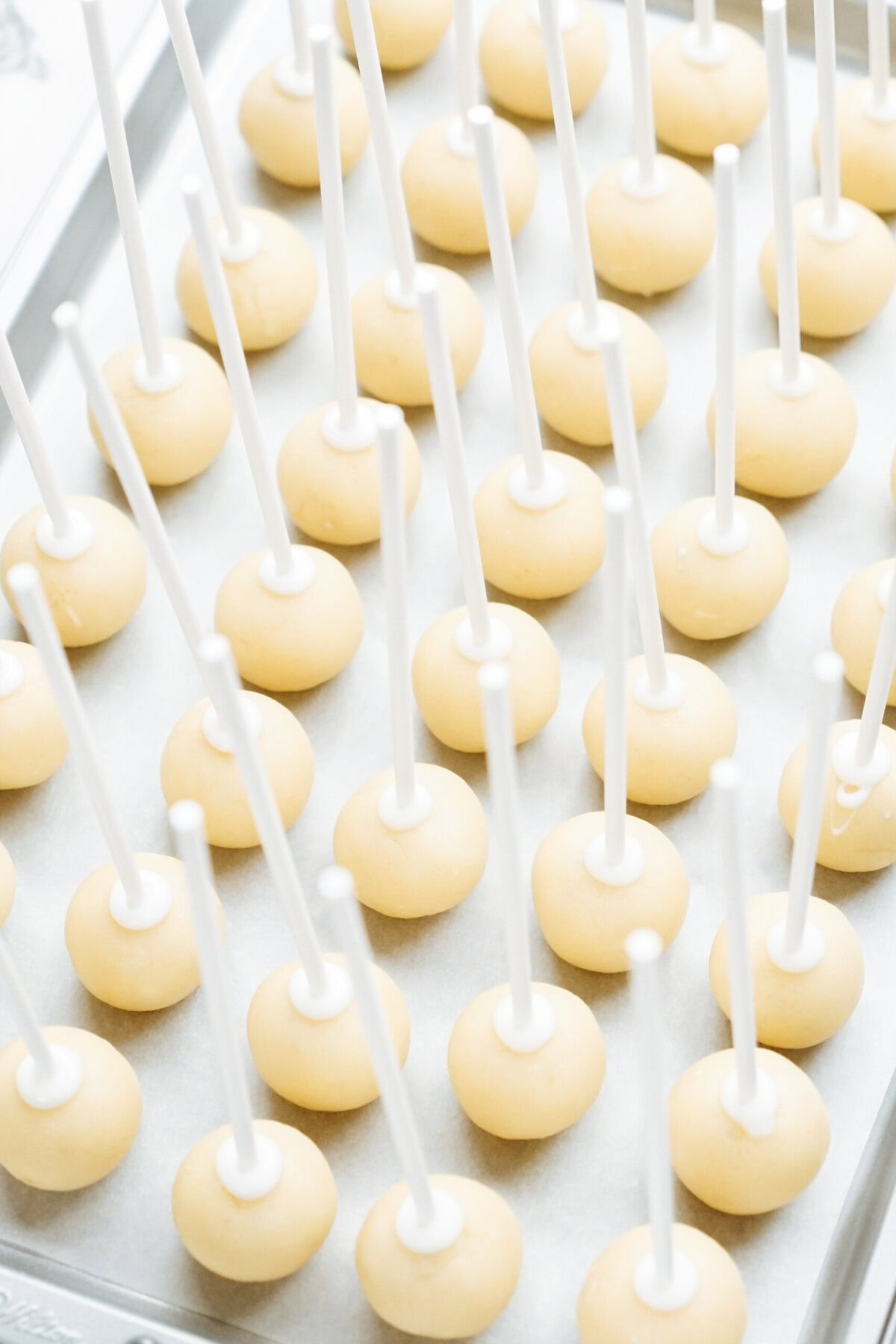 A tray of Christmas cake pops arranged evenly on white parchment paper, each with a festive white stick inserted.