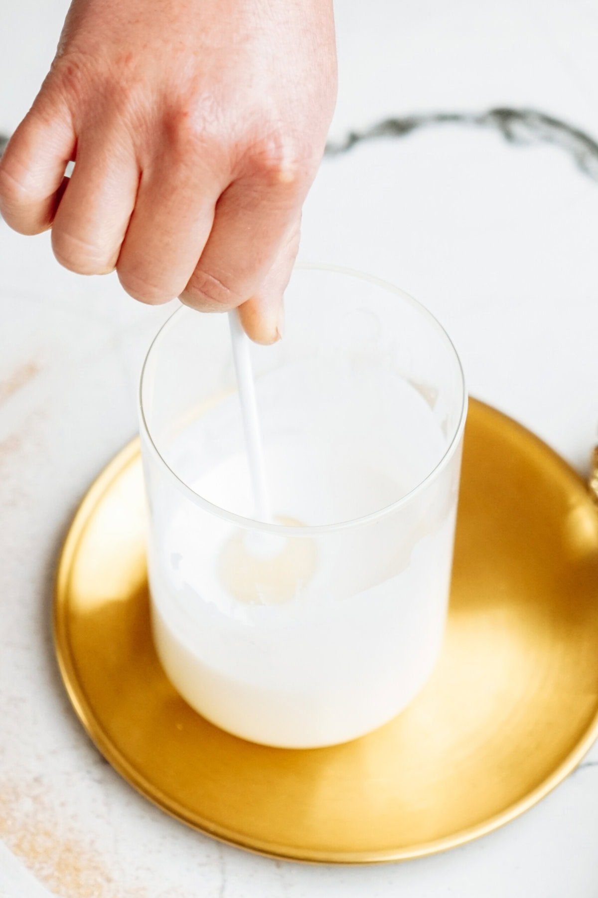 Hand stirring a white liquid in a glass placed on a golden saucer, reminiscent of preparing festive treats like Christmas cake pops.