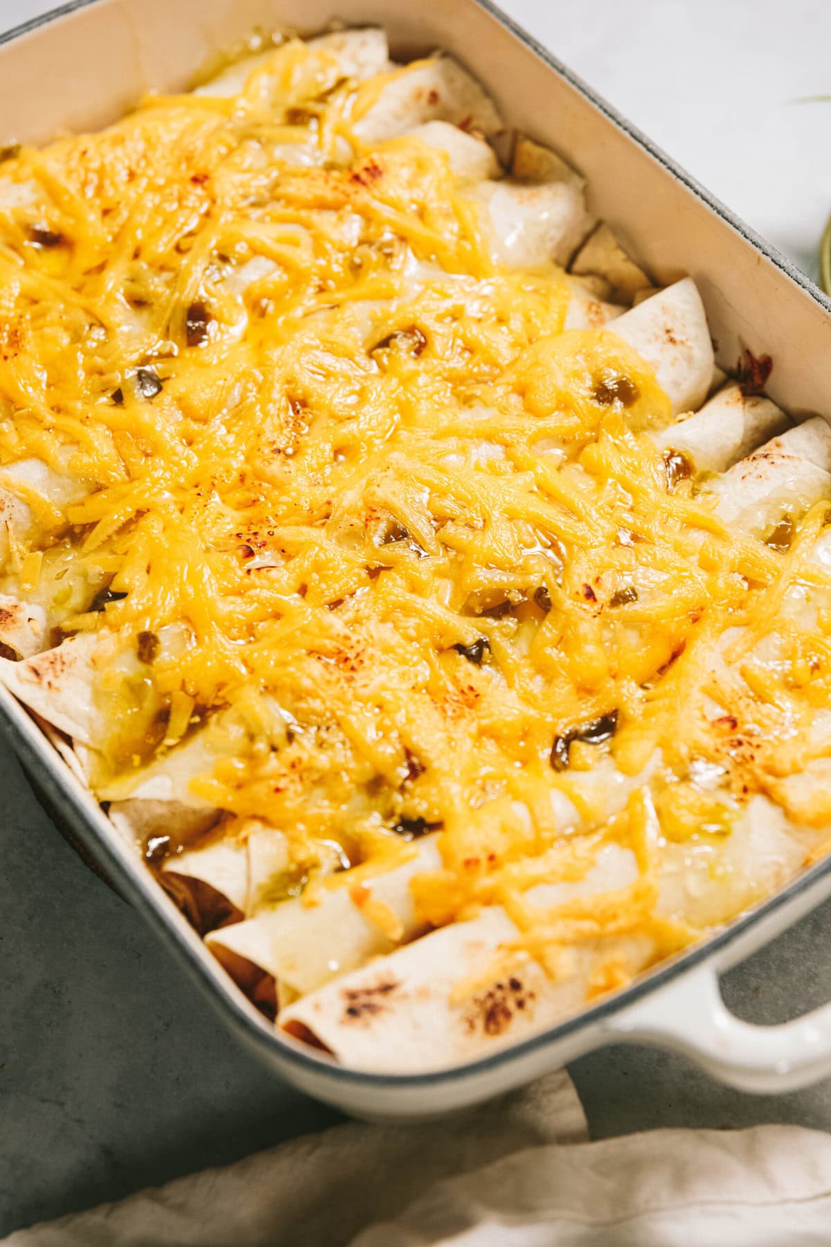 A casserole dish filled with baked enchiladas topped with melted cheese and a green chili sauce.