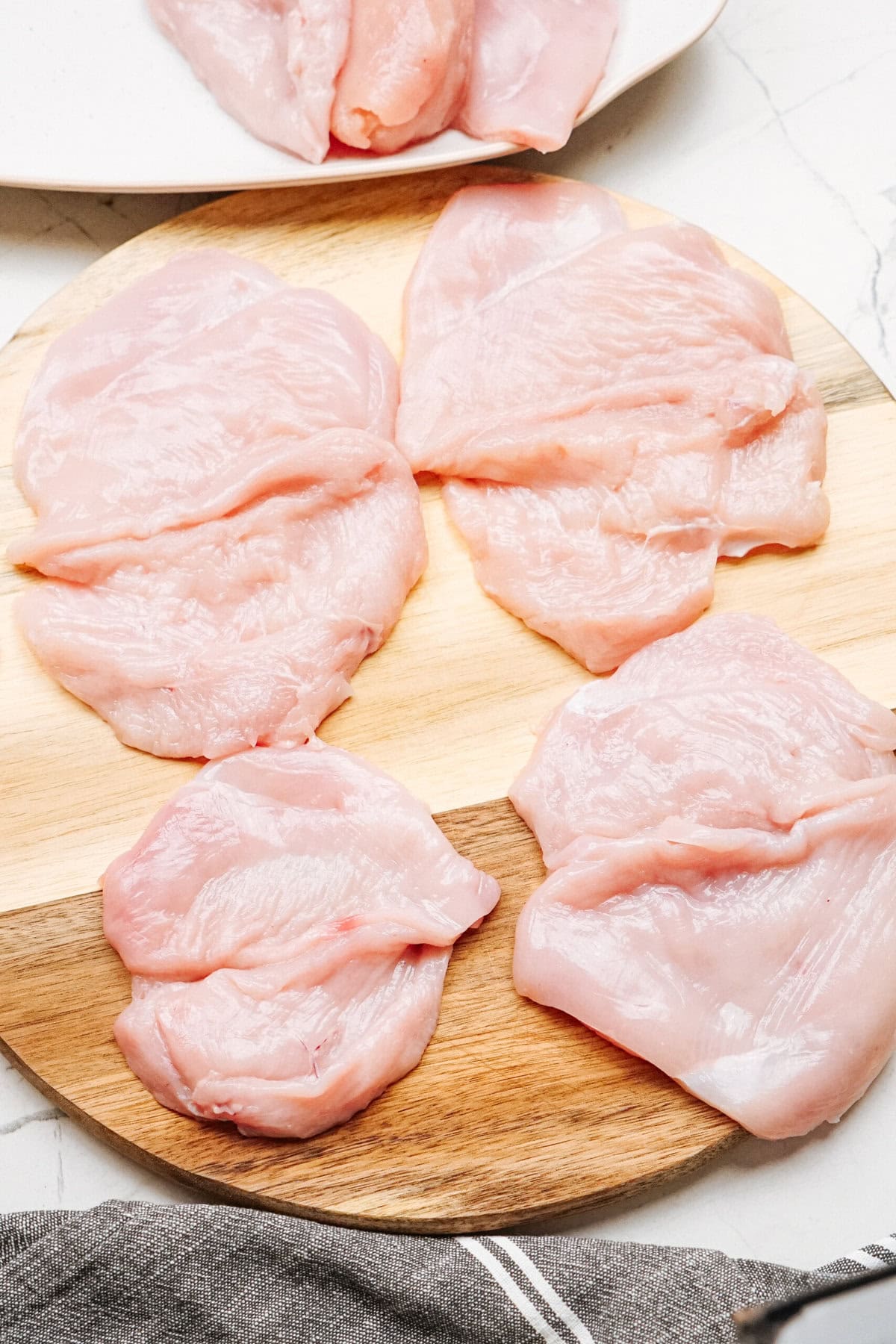 Slices of raw chicken breast arranged on a wooden cutting board.