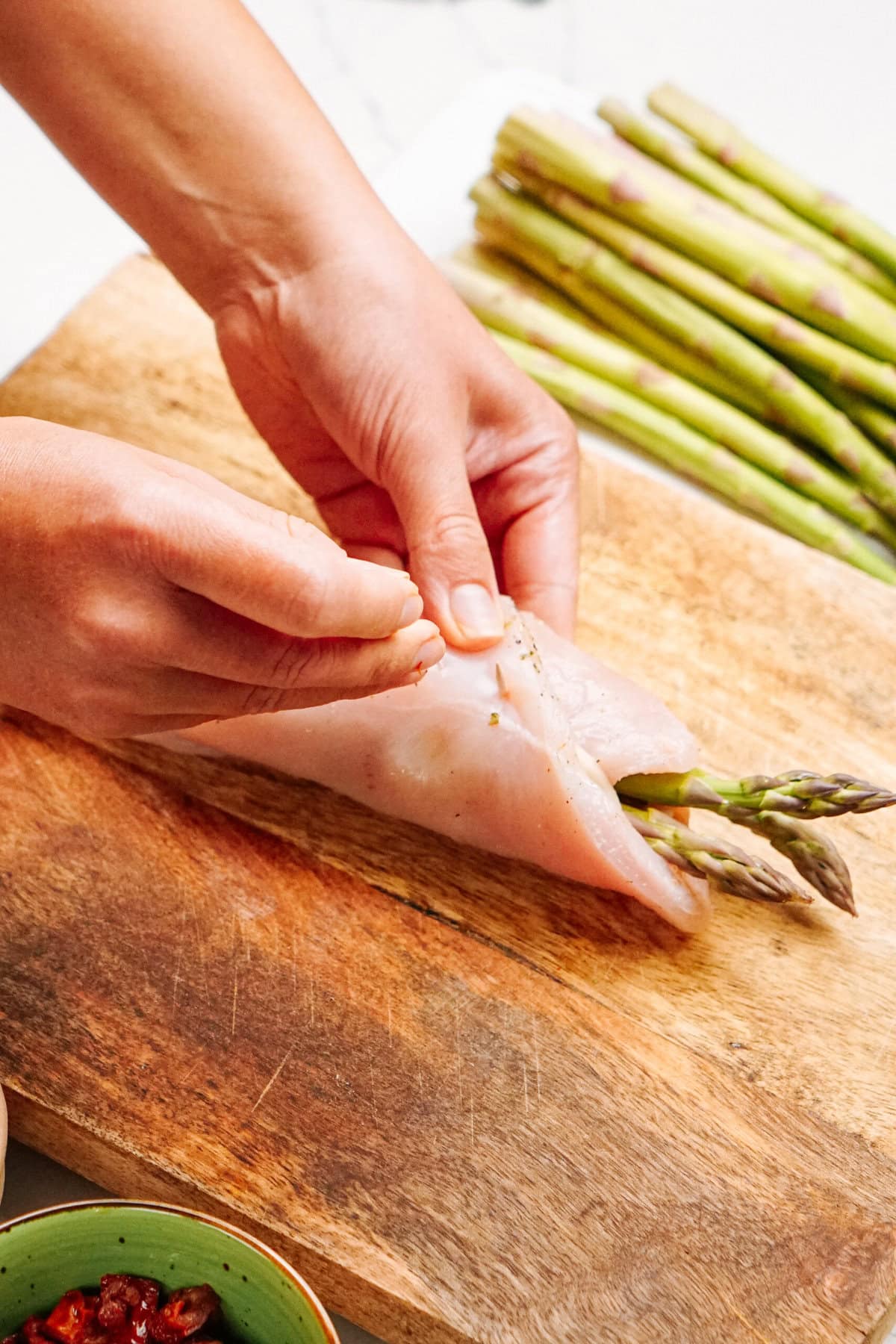 Person rolling asparagus in a chicken breast on a wooden board.