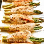 Baked chicken breasts rolled around asparagus, seasoned with pepper, arranged on a baking sheet.