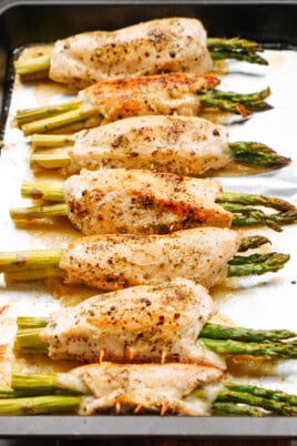 Baked chicken breasts rolled around asparagus, seasoned with pepper, arranged on a baking sheet.