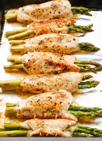 Baked chicken breasts rolled around asparagus, seasoned with pepper, arranged on a baking sheet.