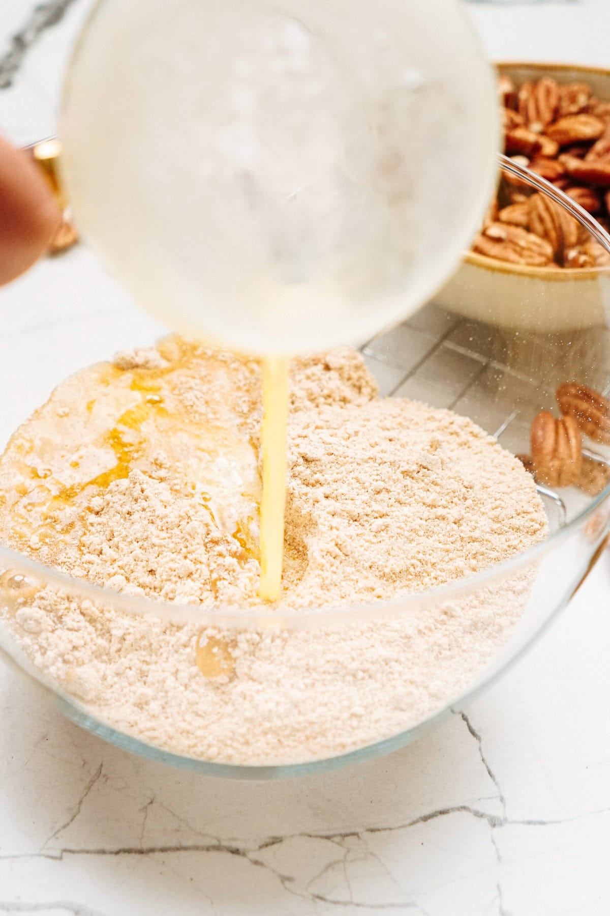 A bowl with flour mixture is being combined with liquid, next to a bowl containing pecans.