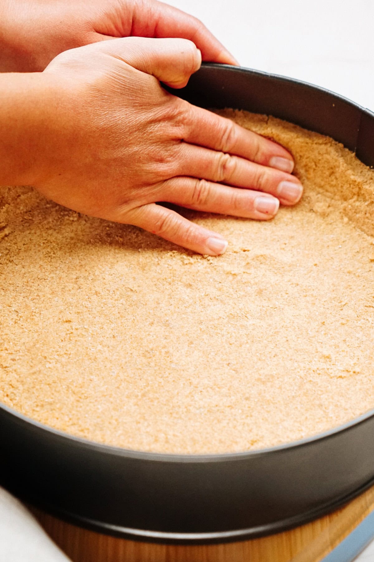 Hands pressing a crumbly pie crust into a round baking pan.