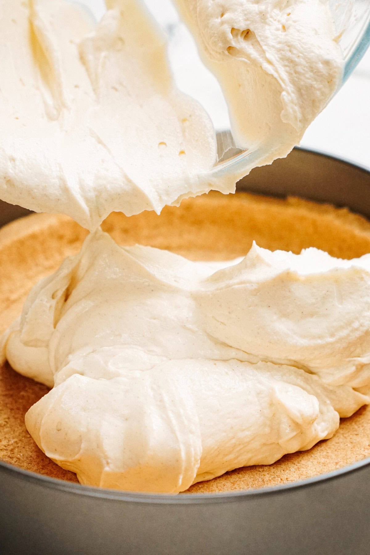 Creamy batter being poured into a round baking pan with a crust base.