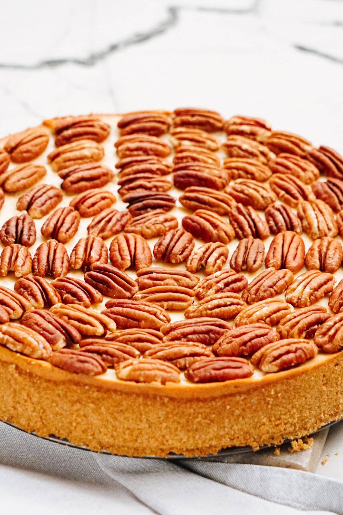 A pecan pie topped with whole pecan nuts on a light background.