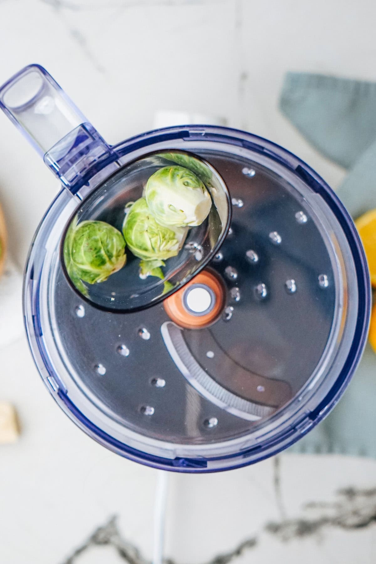 Top view of a food processor with a lid, containing three Brussels sprouts in a measuring cup above it.