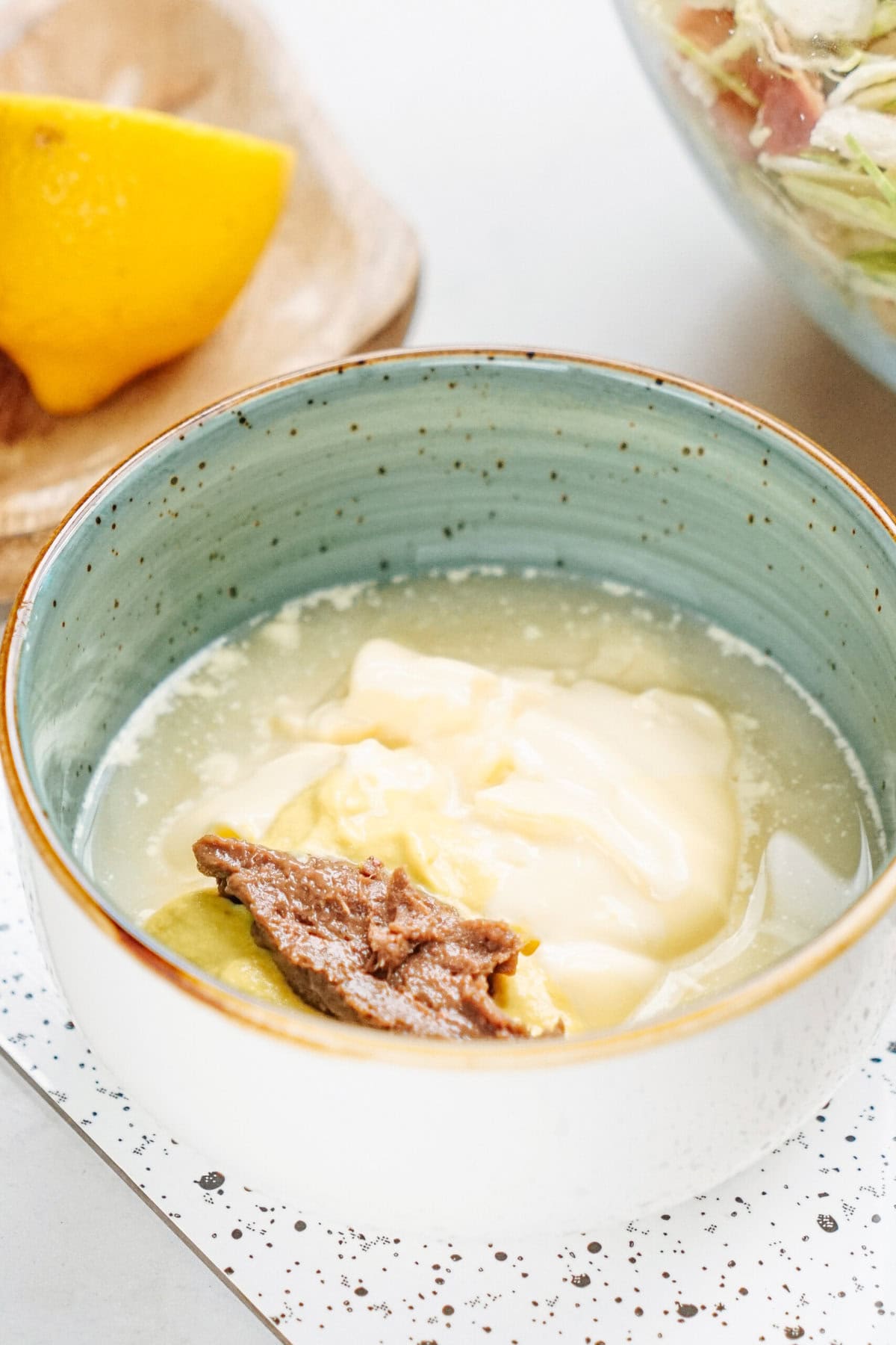 A bowl containing mayonnaise and a dollop of brown paste. A lemon wedge is in the background.