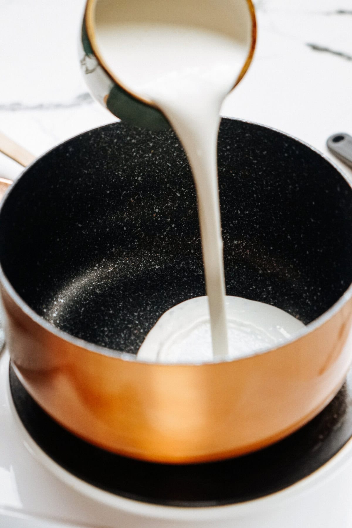 Pouring milk into a copper saucepan on a stovetop.