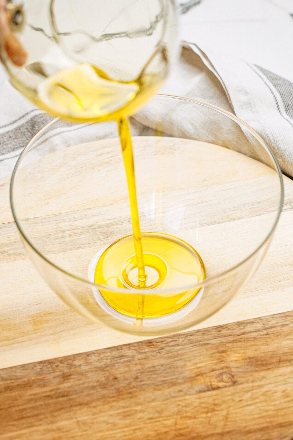 Golden yellow liquid being poured into a glass bowl on a wooden surface.