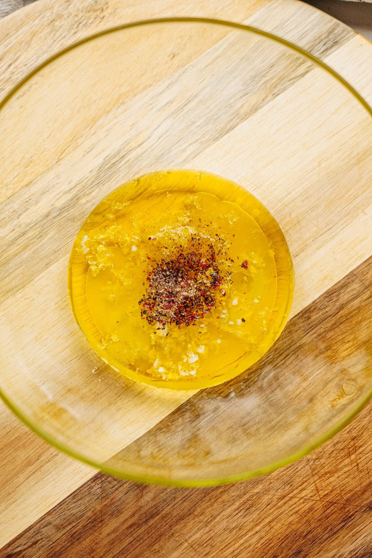 A bowl containing a mixture of olive oil, minced garlic, and assorted spices on a wooden surface.