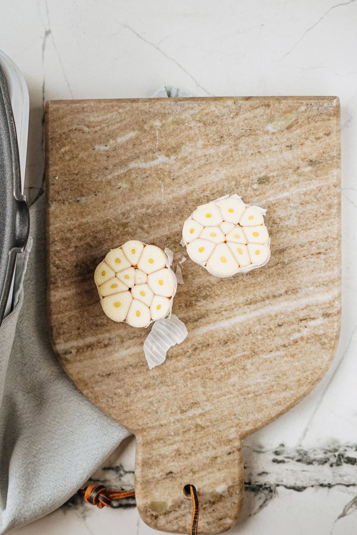 Two halved garlic bulbs on a wooden cutting board placed on a marble surface.