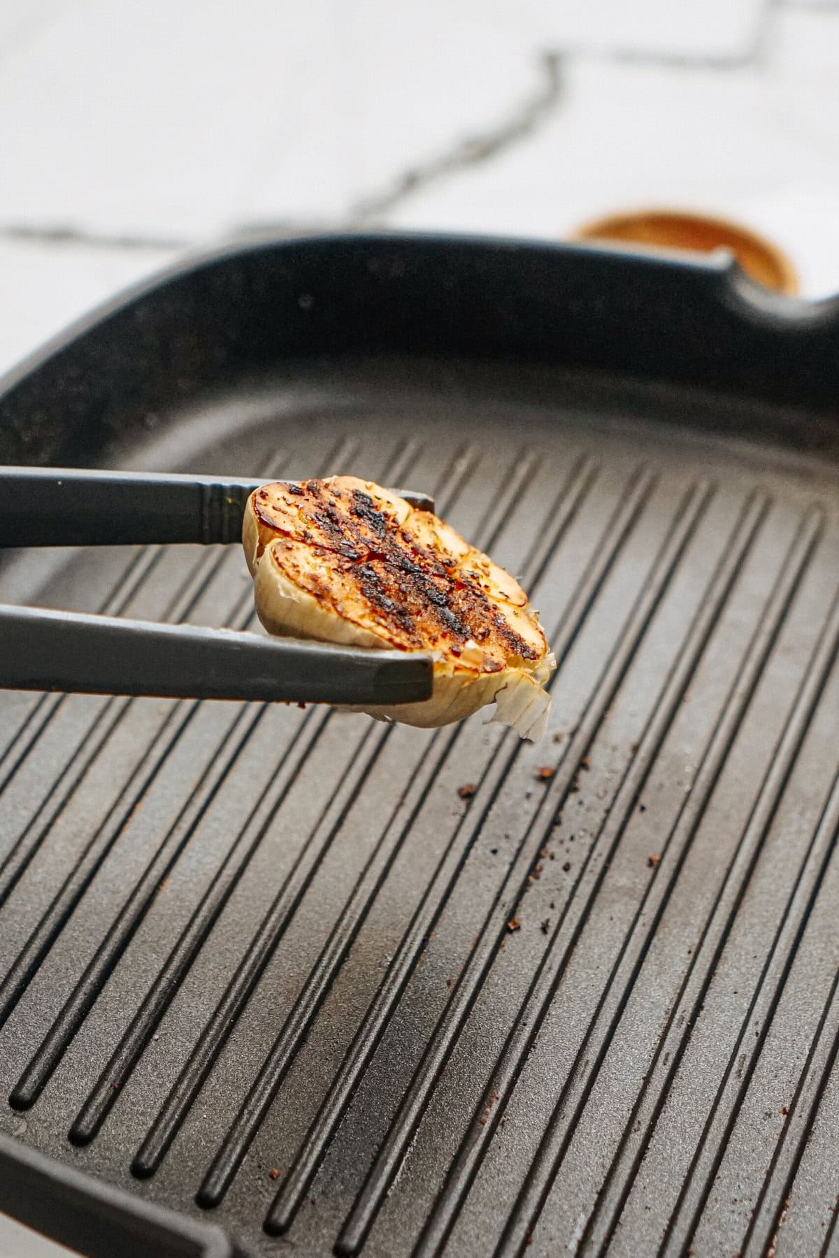 Tongs holding a grilled piece of halloumi over a ridged grill pan.