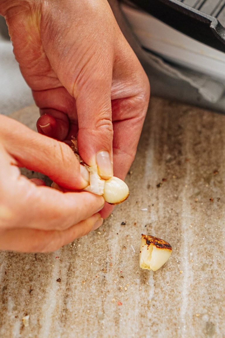 Hands peeling a roasted garlic clove on a speckled countertop.