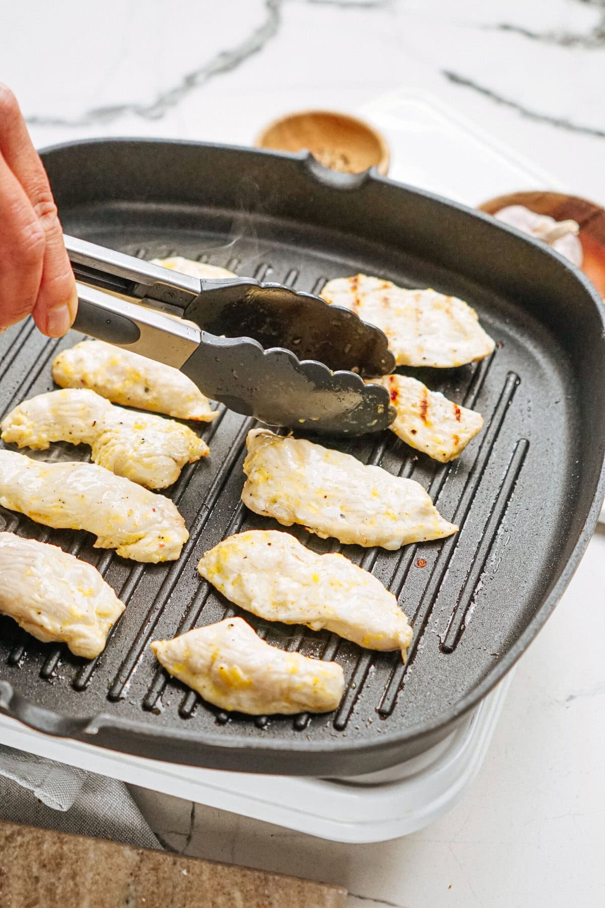 Chicken strips being grilled on a stovetop grill pan, handled with tongs.