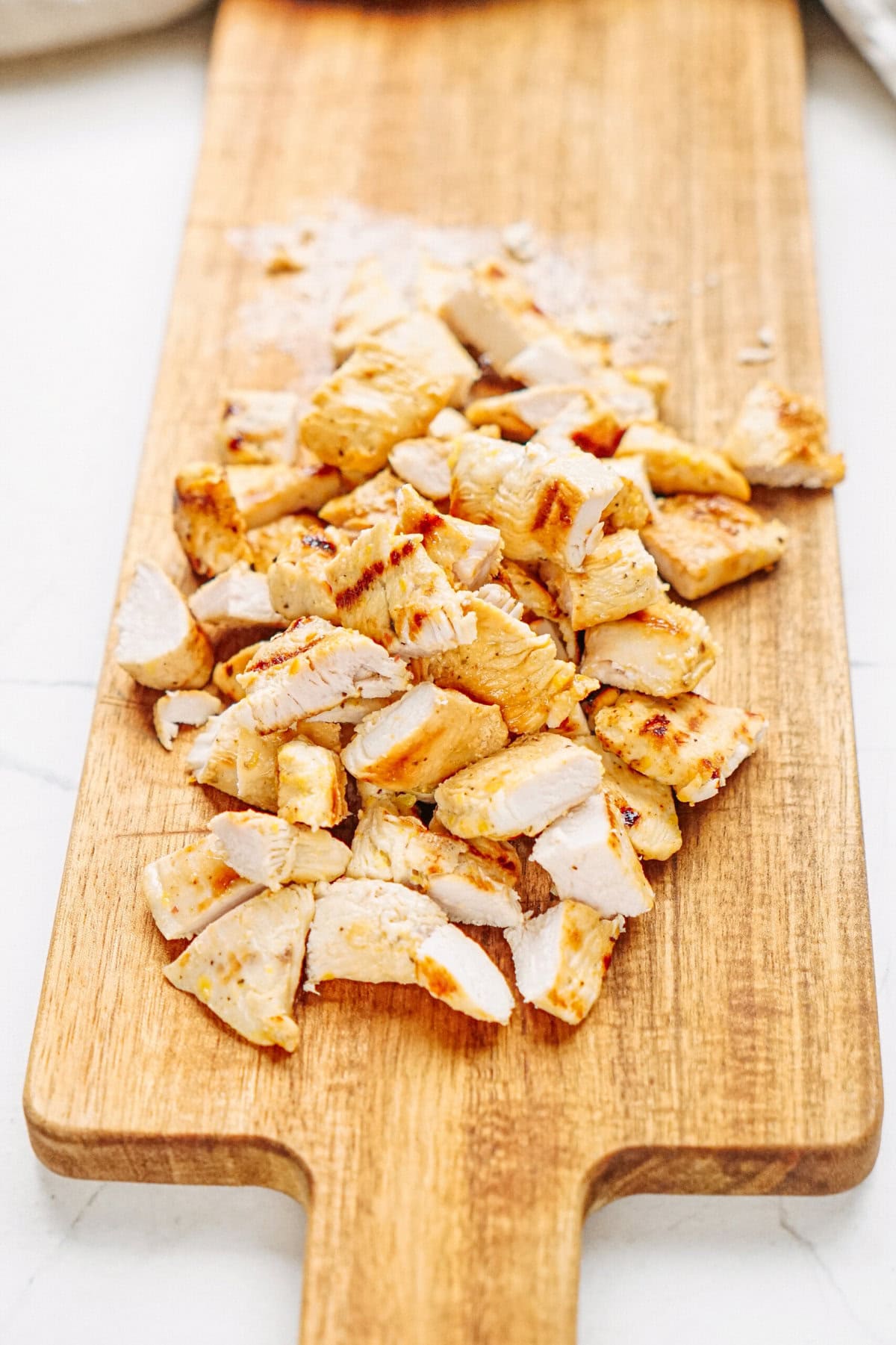 Chopped grilled chicken pieces on a wooden cutting board.