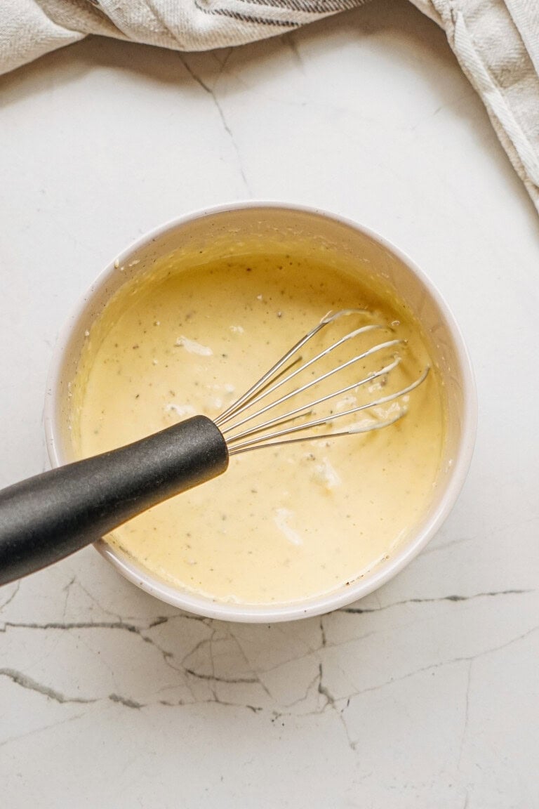 A bowl of creamy batter with a whisk inside, placed on a marble surface.