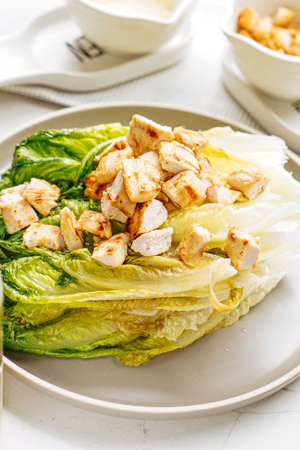 Plate of chopped chicken on a bed of romaine lettuce, with small bowls in the background.