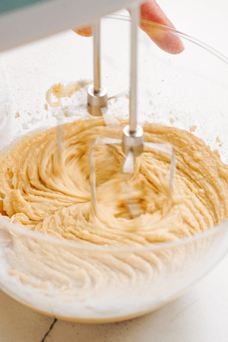 Close-up of a hand mixer blending creamy peanut butter cookie dough dip in a glass bowl.