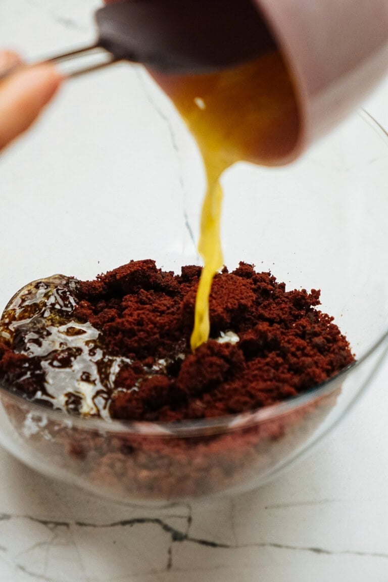 Melted butter being poured into a bowl of chocolate crumbles on a marble countertop.