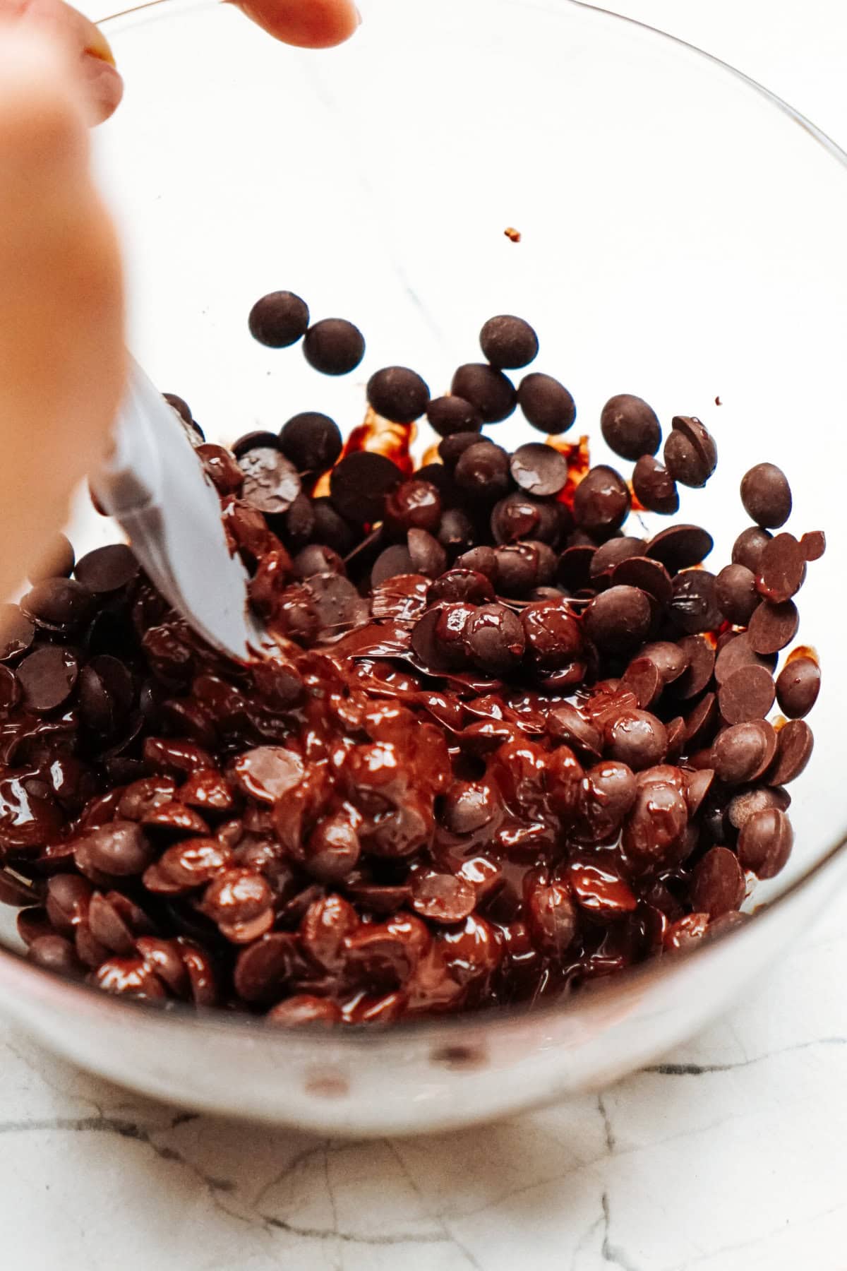 A bowl of semi-melted chocolate chips being stirred with a spoon.