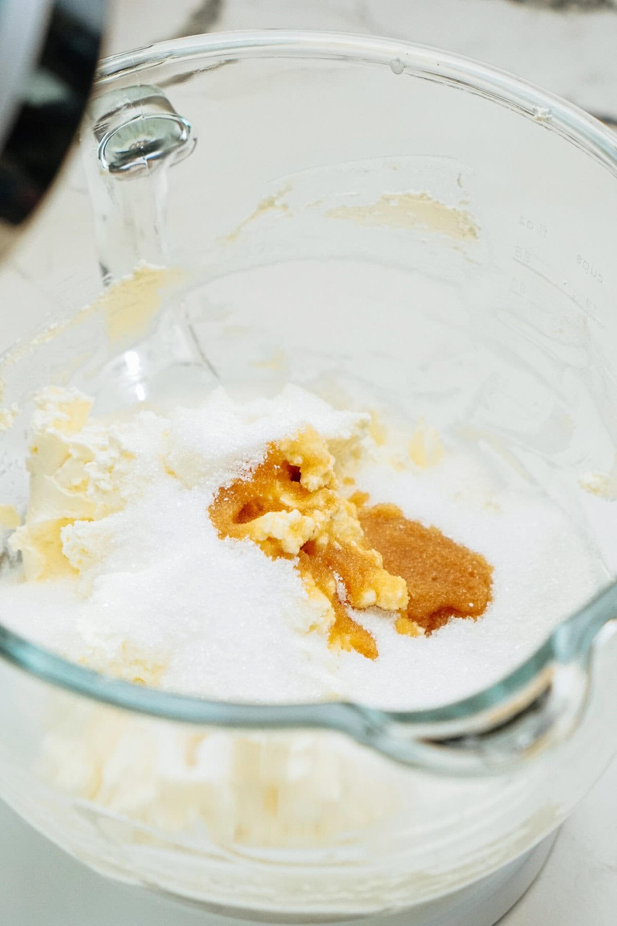 A glass mixing bowl contains butter, sugar, and vanilla extract, prepared for mixing.