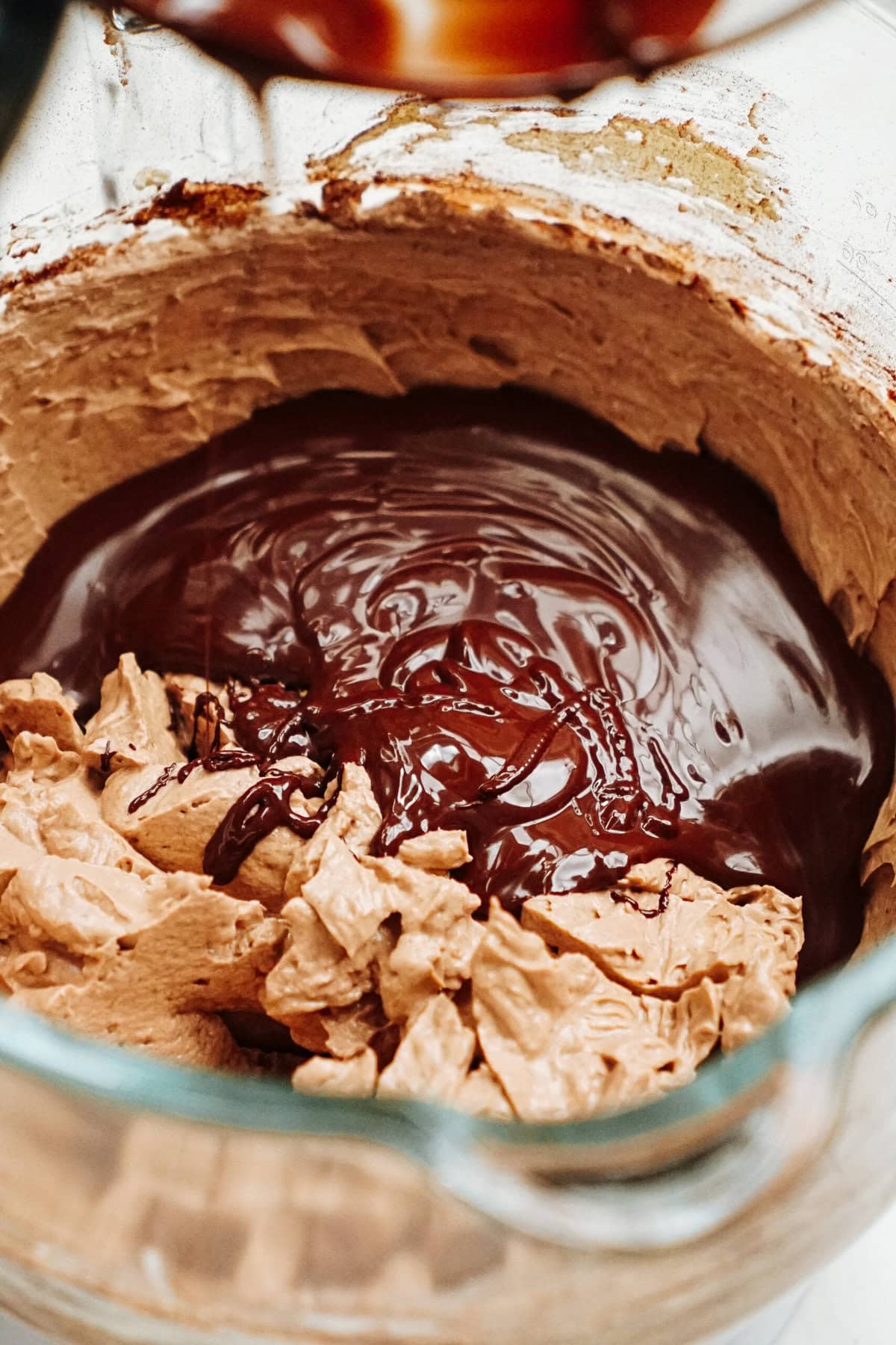 Chocolate being poured into a mixing bowl with a creamy, light brown mixture.