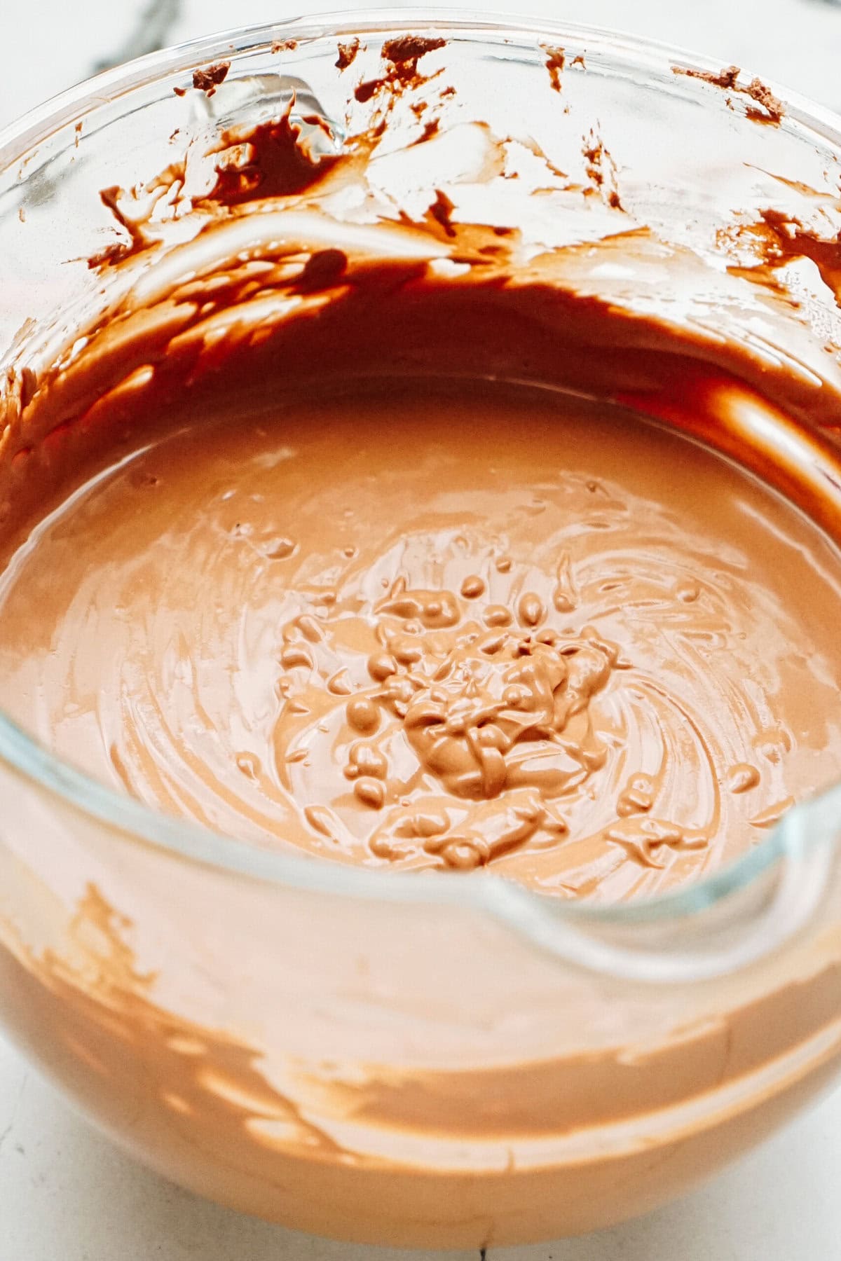 A glass mixing bowl filled with smooth, glossy chocolate cake batter on a white countertop.