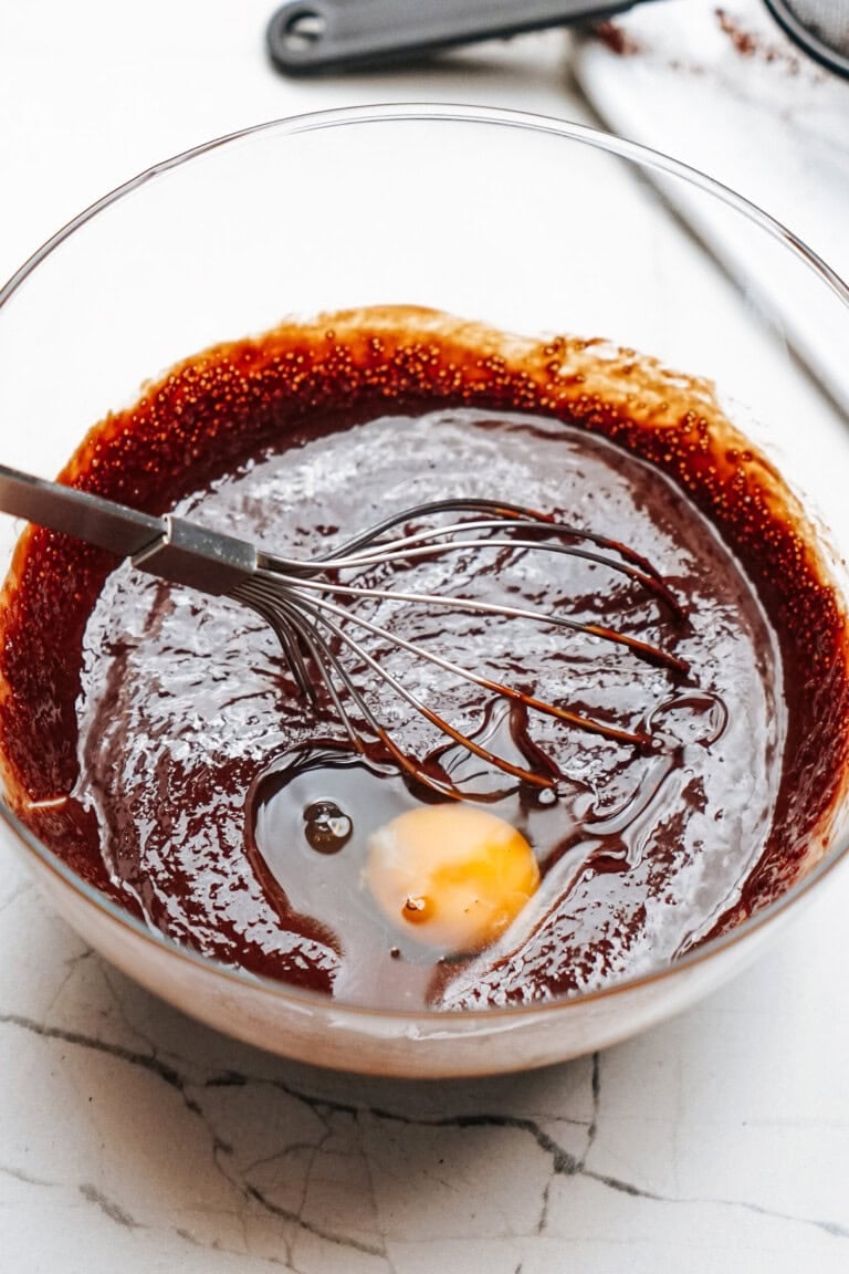 A glass bowl with a chocolate mixture and a cracked egg, being whisked together.