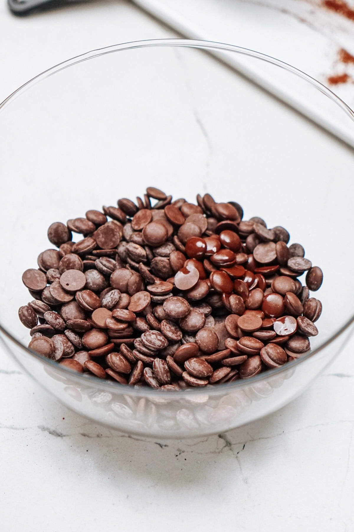 A glass bowl filled with dark chocolate chips on a white surface.