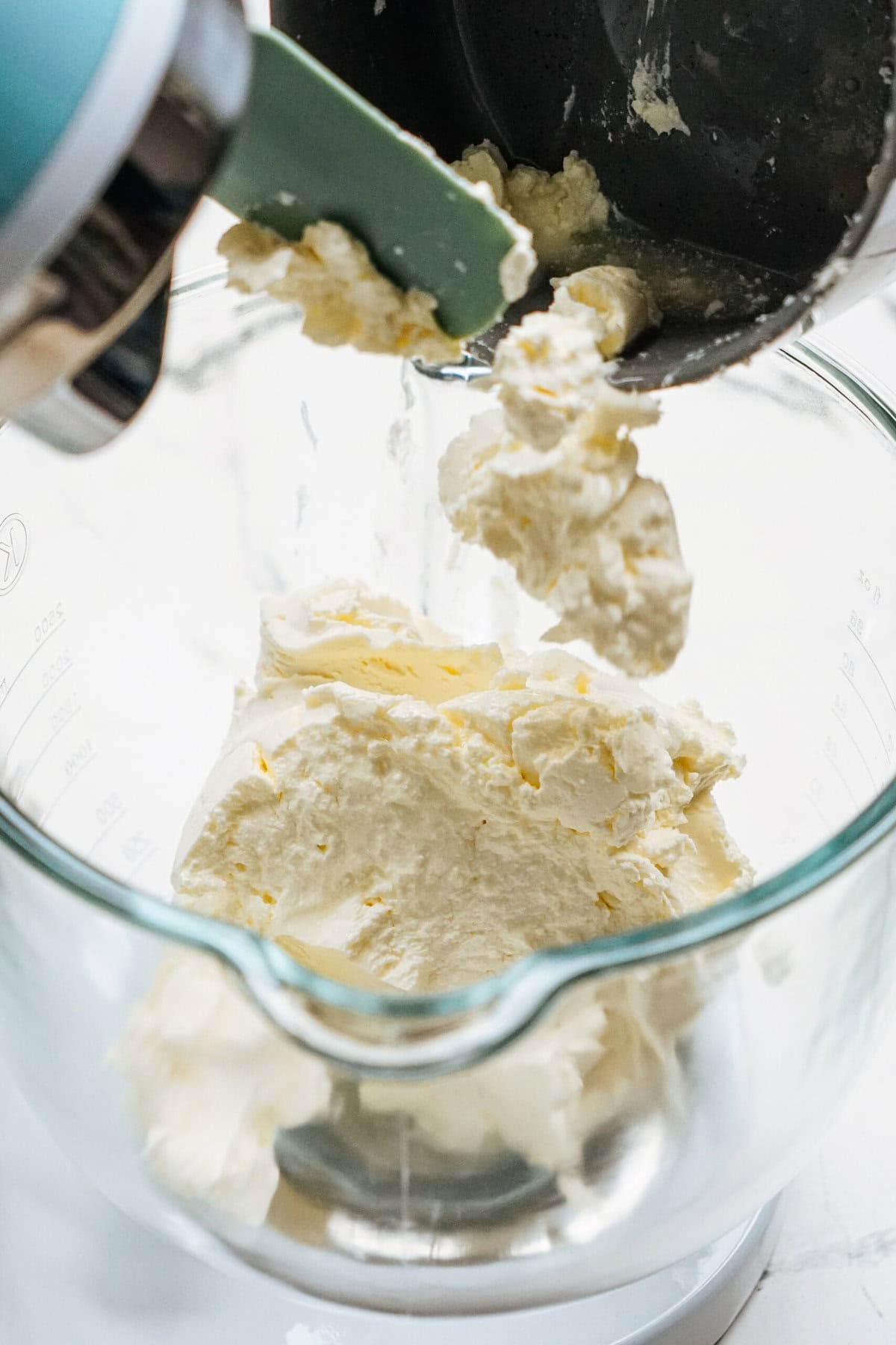 Butter and cream cheese being mixed in a glass bowl with a spatula.