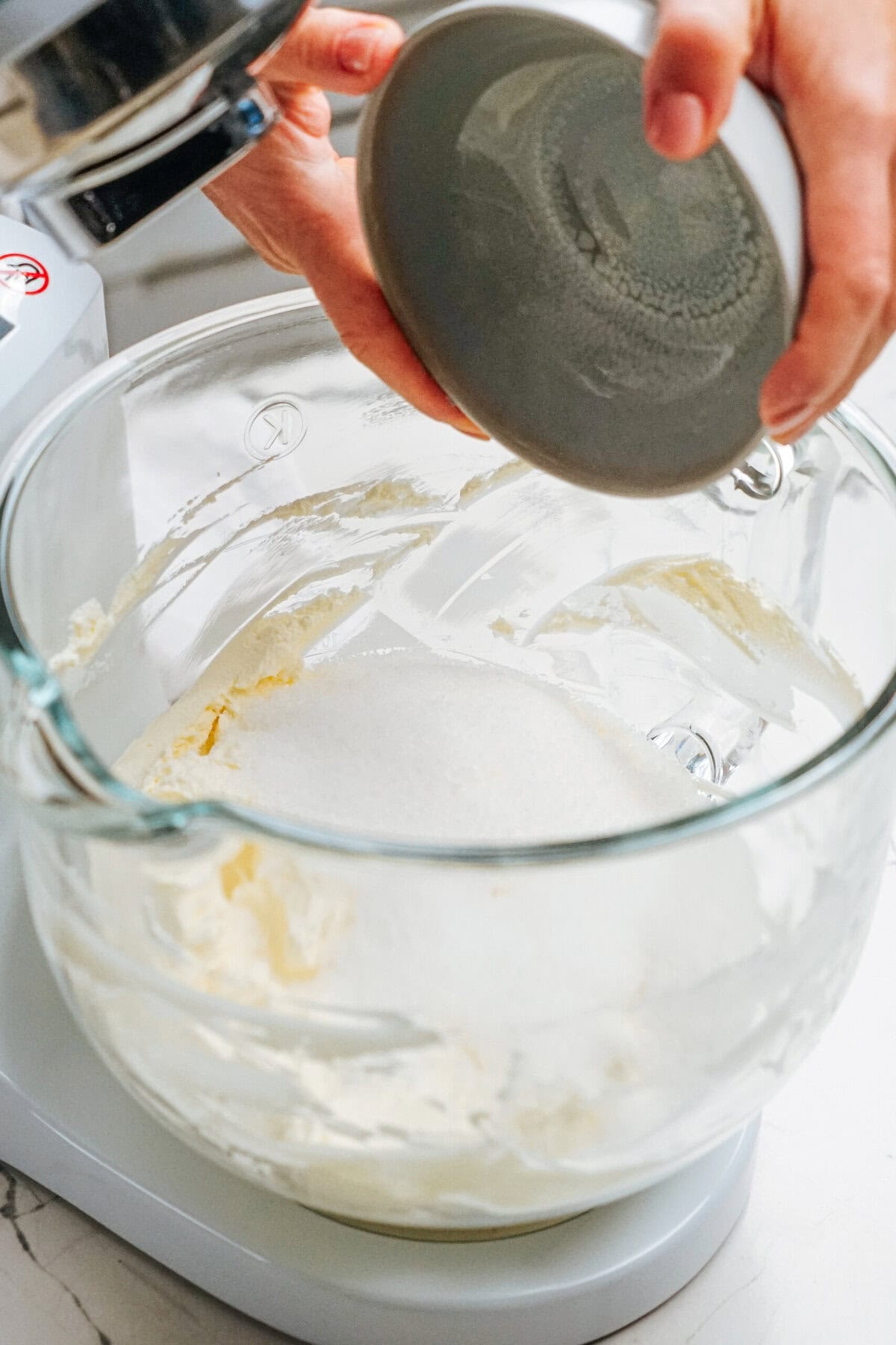 Person adding sugar into a mixing bowl with cream using a stand mixer.