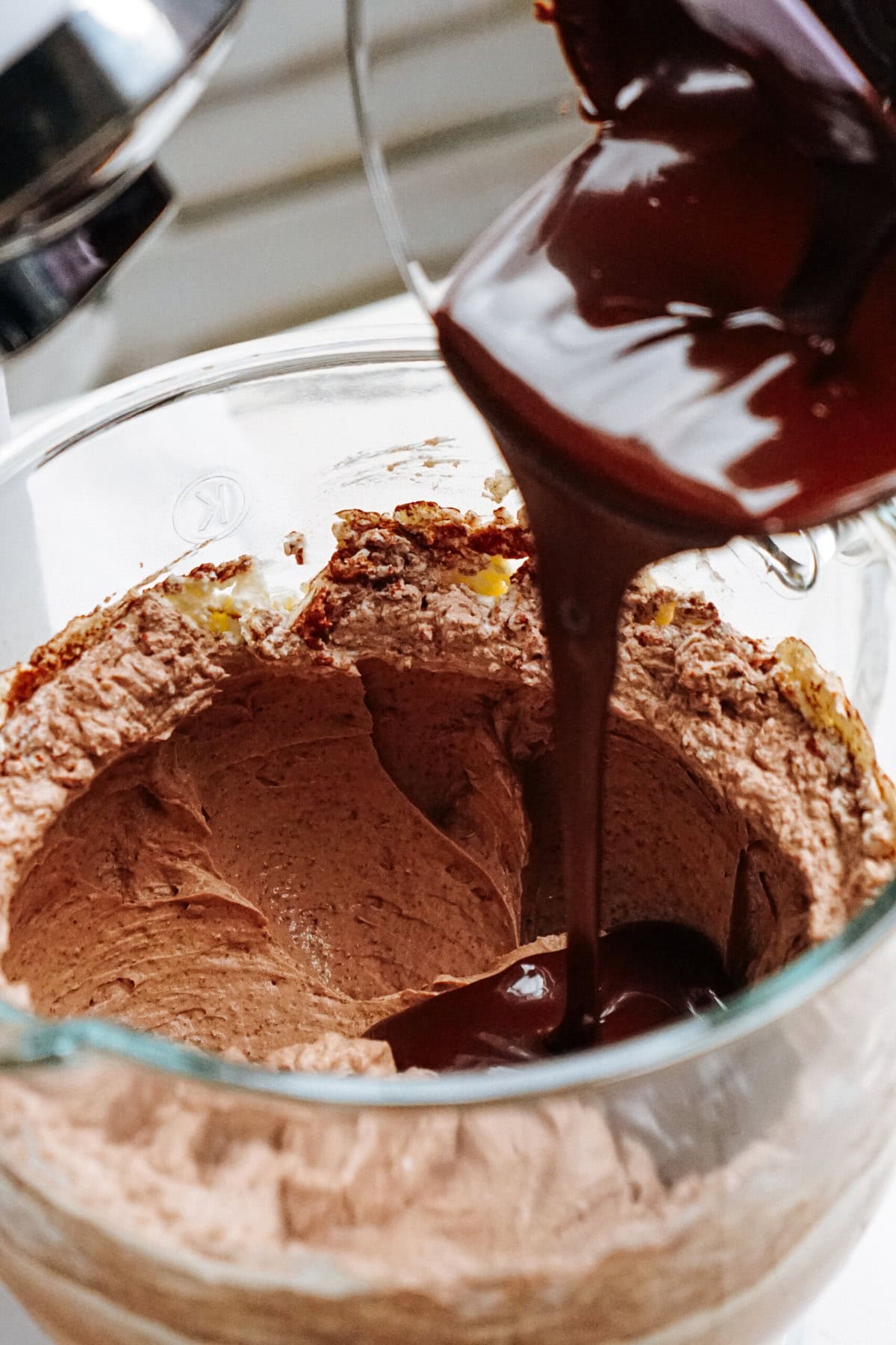 Chocolate sauce being poured into a bowl of chocolate mousse in a glass container.