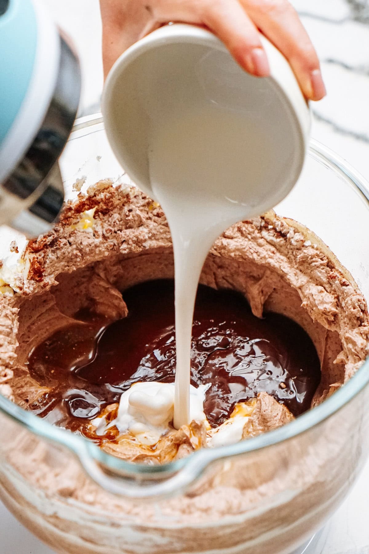 Milk being poured into a mixing bowl containing a chocolate batter mixture.