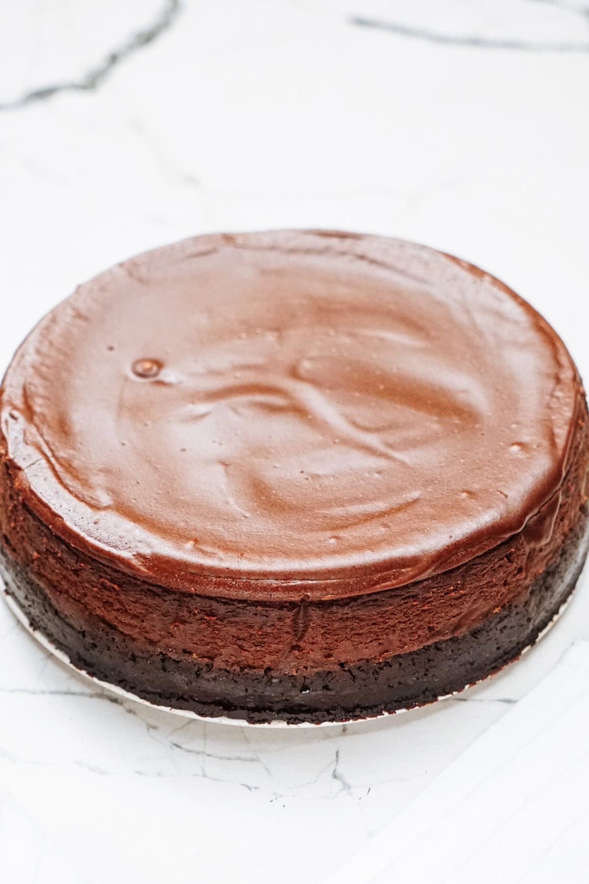 A whole chocolate cheesecake on a white marble surface.