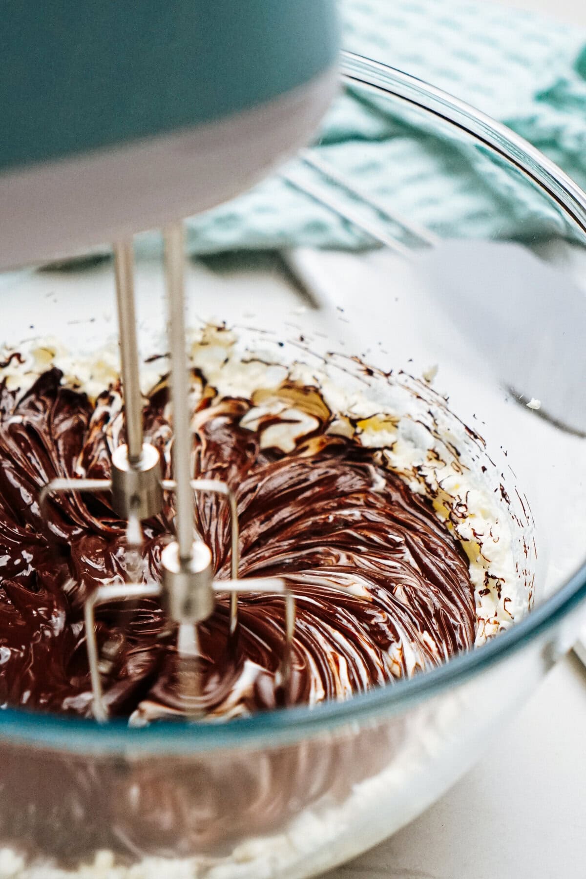 The electric mixer whirs as it blends chocolate and cream in a glass bowl, crafting the perfect chocolate mousse on the countertop.