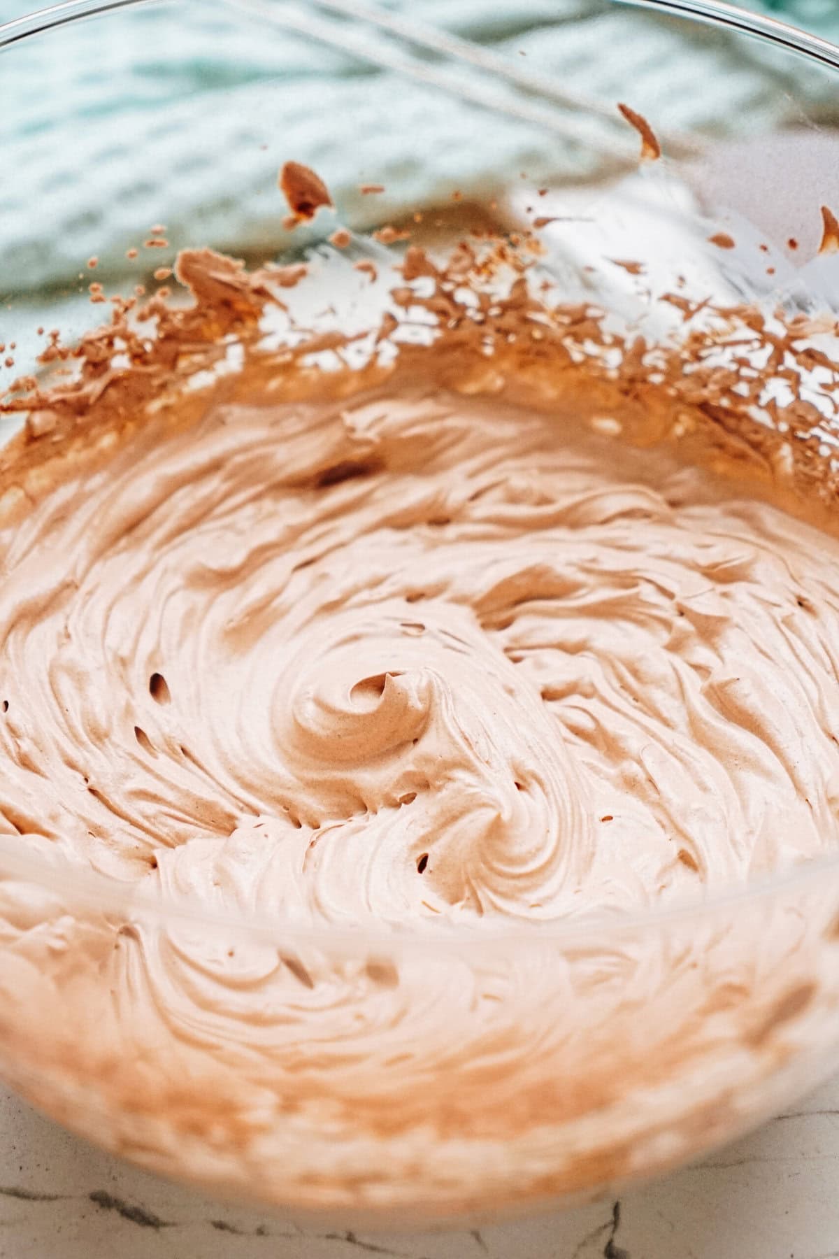 A glass bowl with light brown whipped cream swirled inside, resting on a marble countertop.