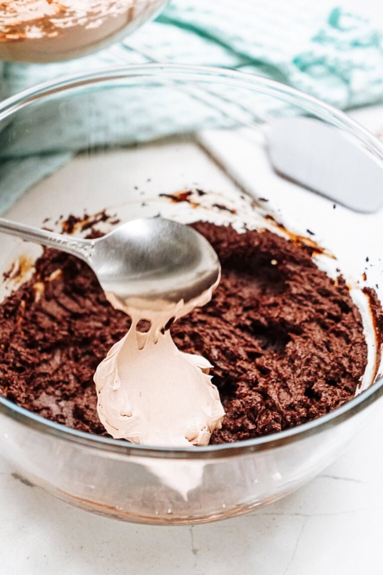 A spoonful of rich chocolate mousse is delicately lifted from a glass bowl, resting on a light surface with a spatula nearby.