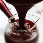 Chocolate sauce being poured into a clear glass jug with a red handle.