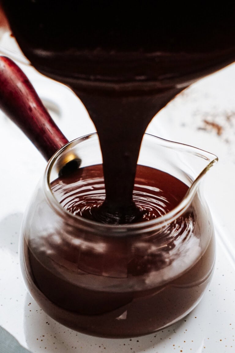 Chocolate sauce being poured into a clear glass jug with a red handle.