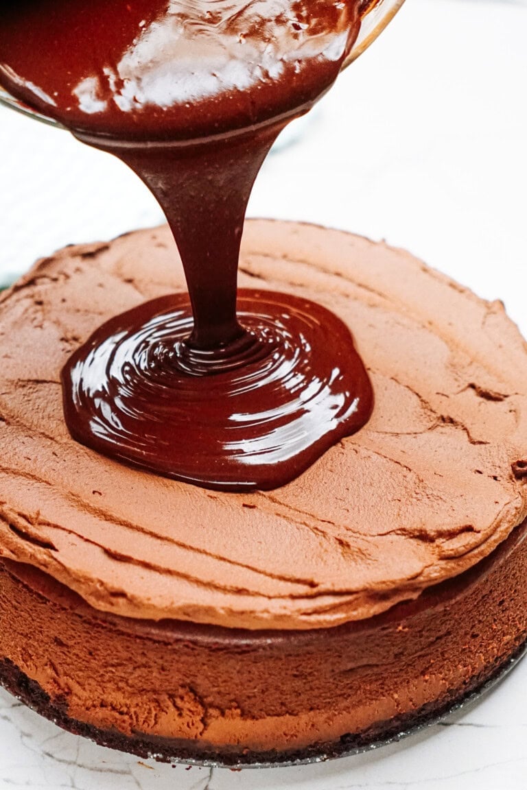 Chocolate ganache is being poured onto a chocolate cake with a smooth frosting base.