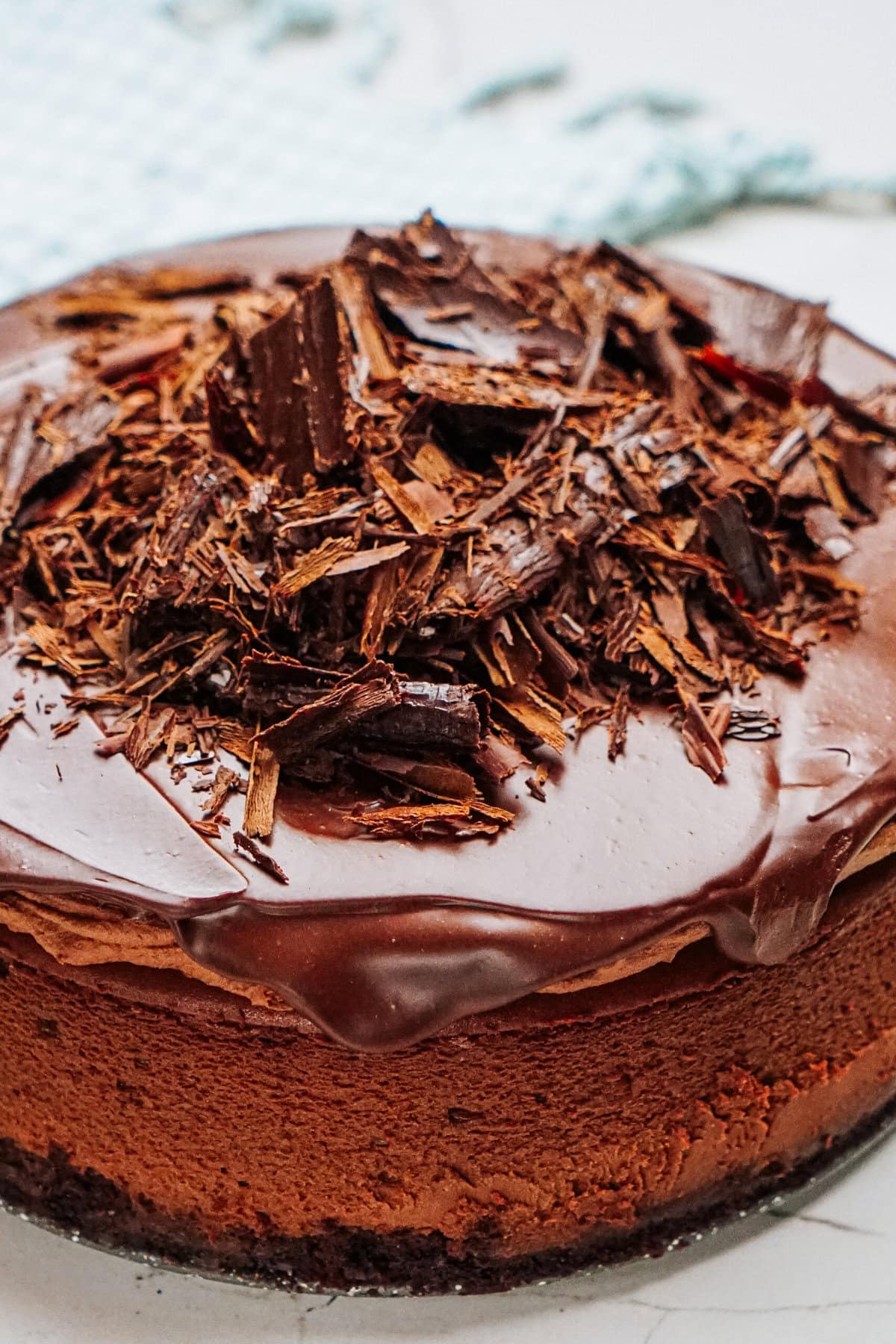 A chocolate cake topped with chocolate shavings, set on a light-colored surface.