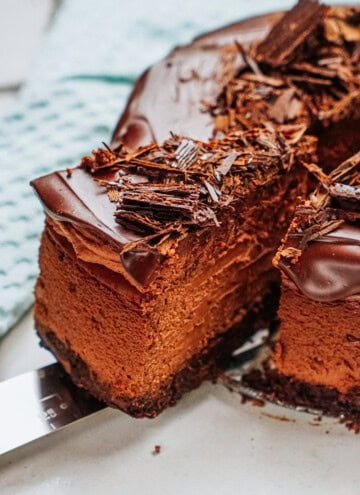 A slice of chocolate cake with creamy layers and a chocolate shavings topping is served on a cake server.