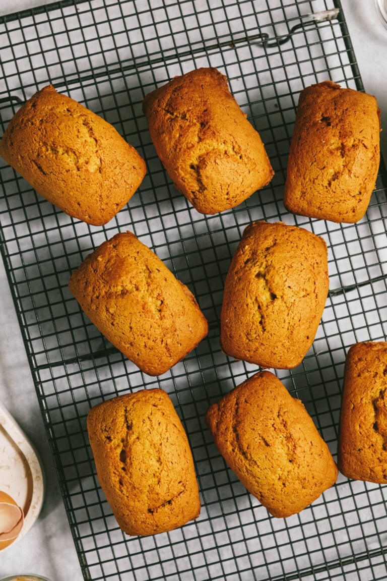 Eight golden brown loaves of bread cooling on a wire rack.